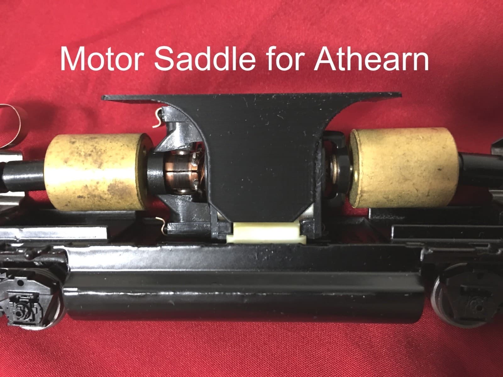 車体を外した機関車の床。2つの円筒のモーターの間に、黒い板の台が付いている。上に「Motor Saddle for Athearn」の文字
