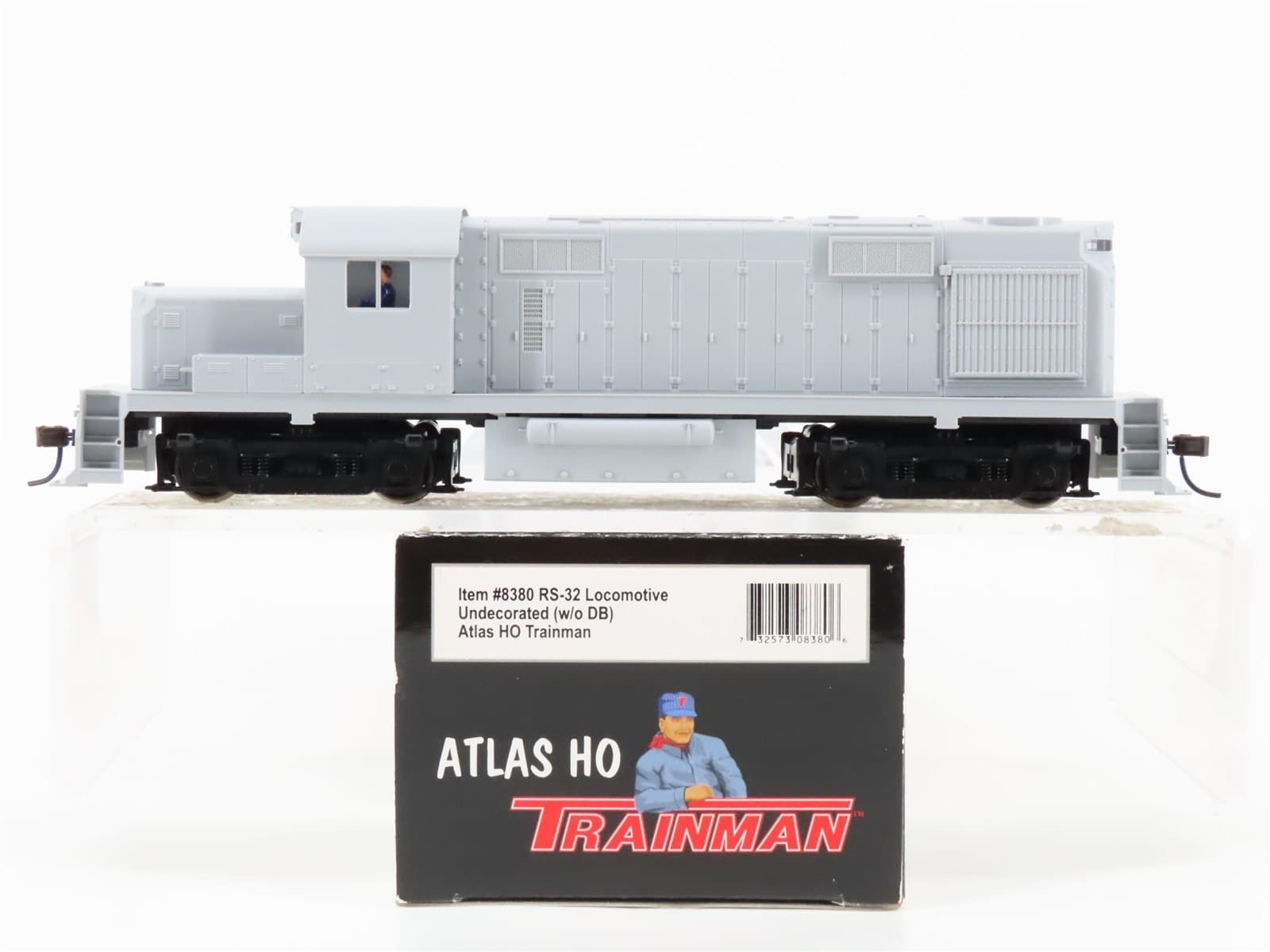 塗装の無い灰色のディーゼル機関車の模型と、手前の黒い箱。箱に「ATLAS HO」「TRAINMAN」と「Item #8380 RS-32 Locomotive Undecorated (w/o DB)」