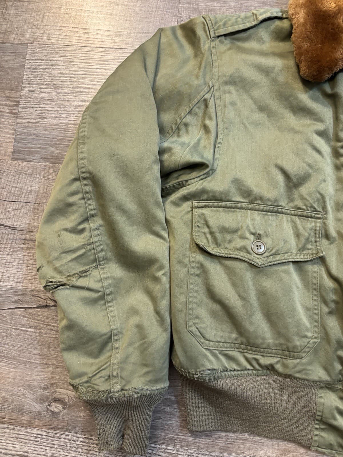 斜めから写したオリーブ色の綿の上着。肩章と胸のフラップ付きのポケット、裾のリブが見える