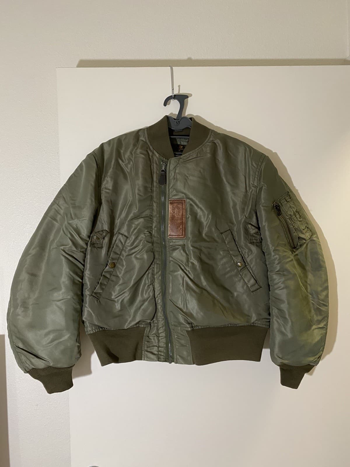 ハンガーに掛けたオリーブのナイロンのジャケット。襟は緑のニット