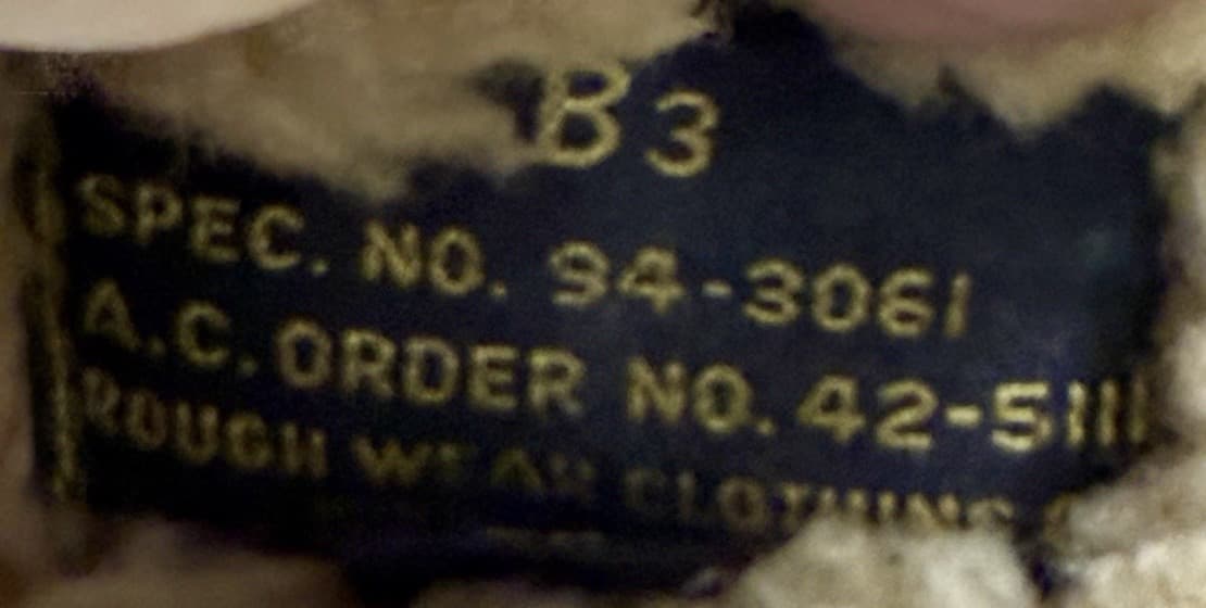 黒い布のラベルに、金色の文字で B3・SPEC. NO. 94-3061・A.C. ORDER NO. 42-511・ROUGH WEAR CLOTHING とある