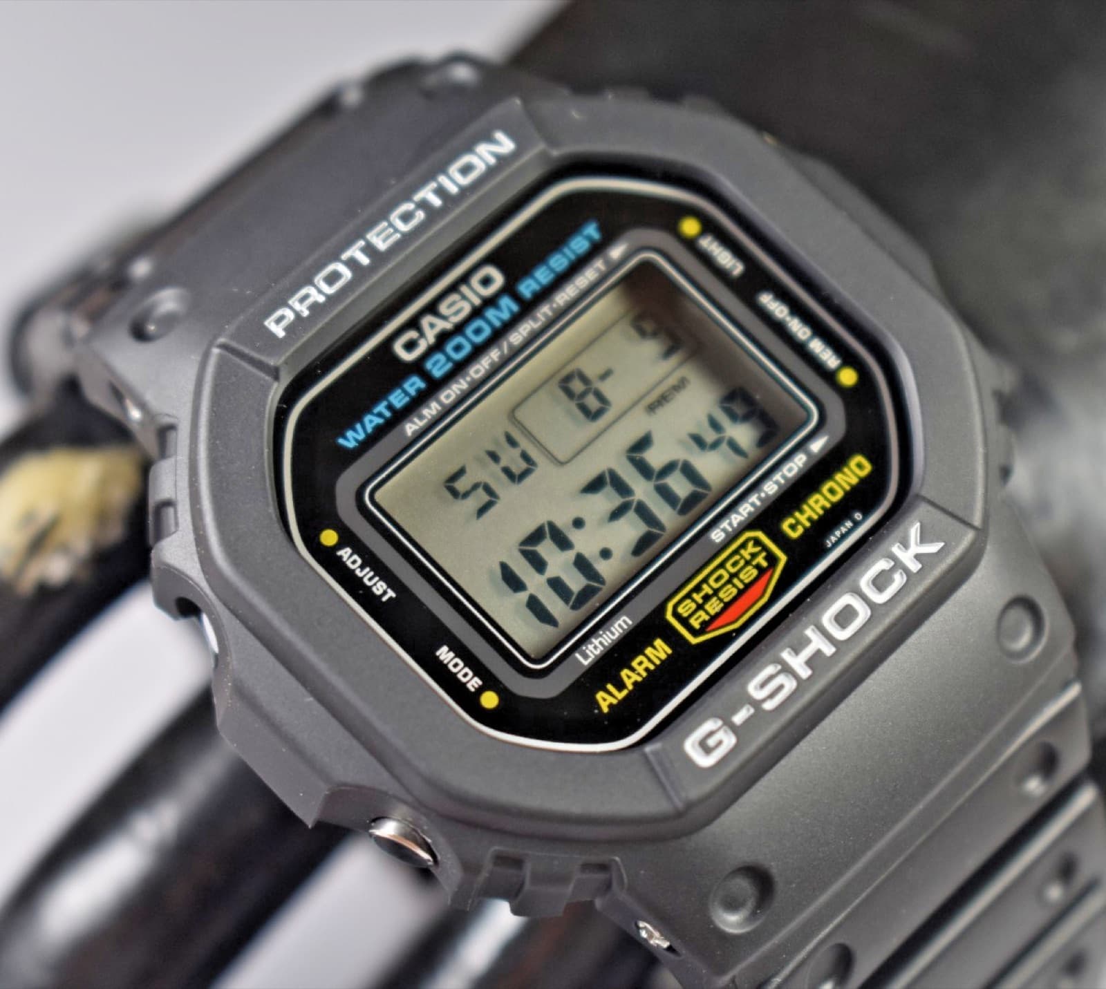 斜めから写した灰色がかった黒い樹脂の角型の時計。上に「PROTECTION」、液晶の上に青い「WATER 200M RESIST」の文字がある
