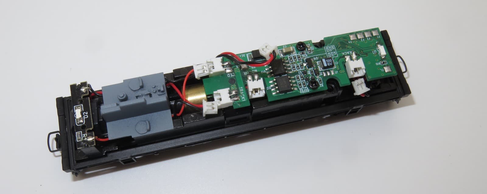Nゲージの模型の車体の床を上から。モーターの横に、ねじで留めた緑のデコーダー基板があり、白い小さなコネクタと赤と黒の配線がつながっている