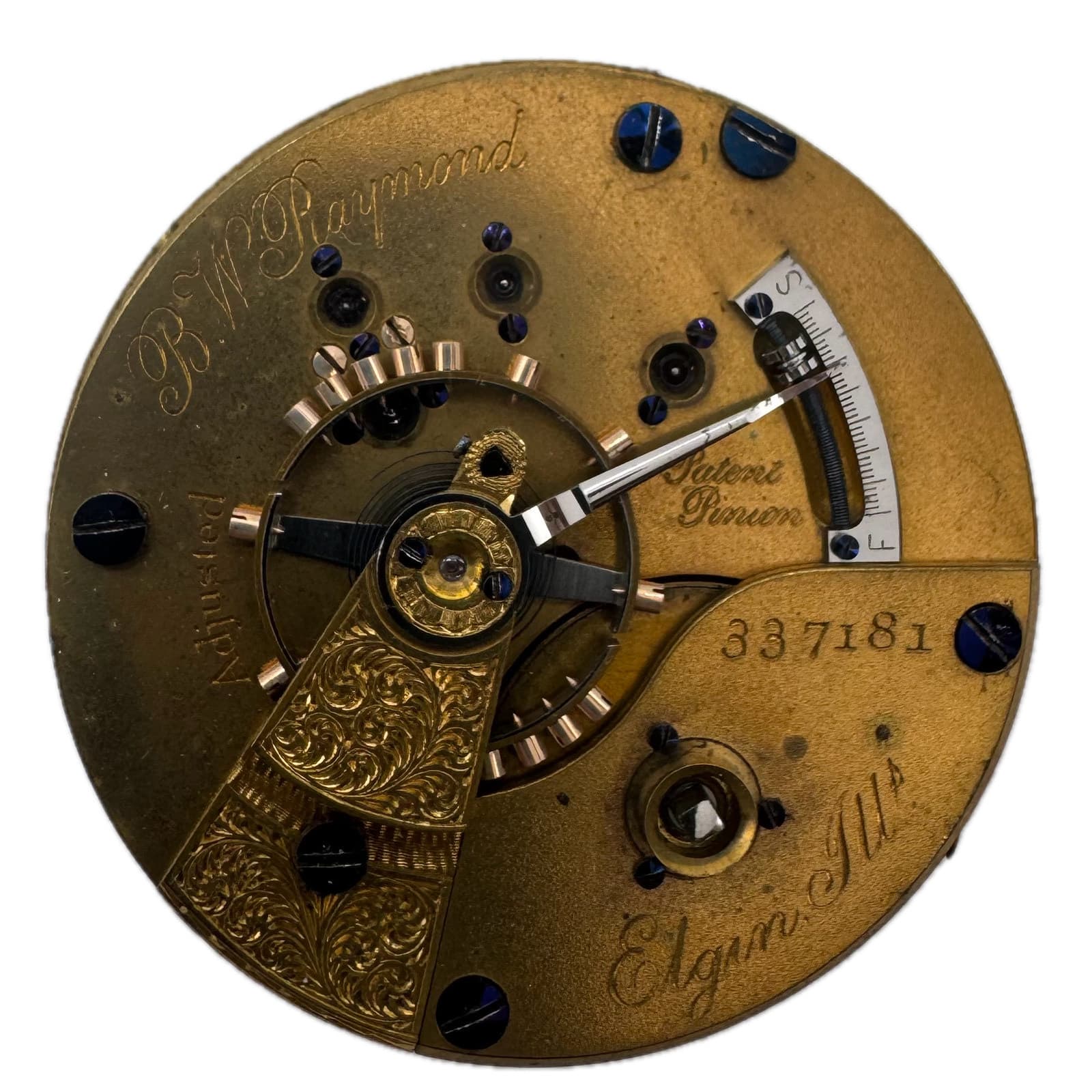 白い背景の、ケースから外した真鍮色の機械。筆記体の「B.W. Raymond」「Patent Pinion」「Elgin Ill.」の刻印と番号、渦巻き模様の彫りがある
