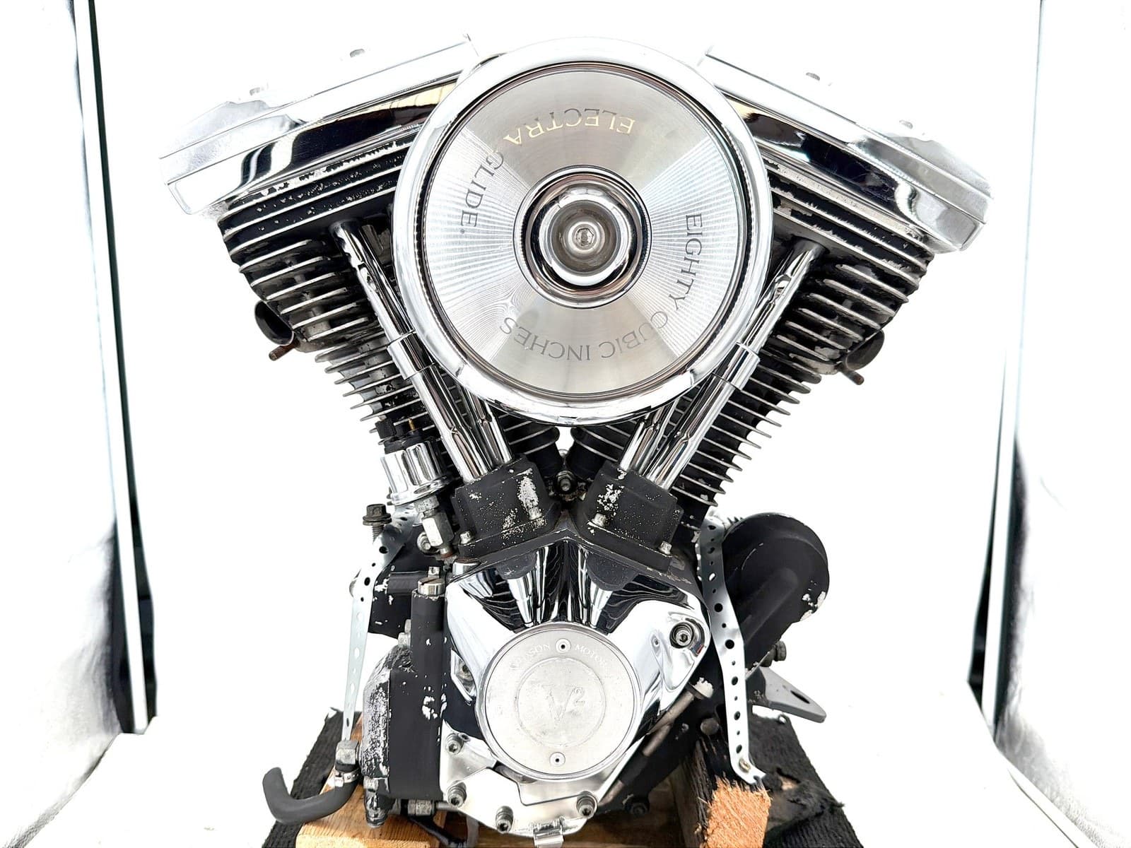 白い背景の前の、めっきのV型2気筒のエンジン。丸いエアクリーナーのカバーに「ELECTRA GLIDE」「EIGHTY CUBIC INCHES」の文字