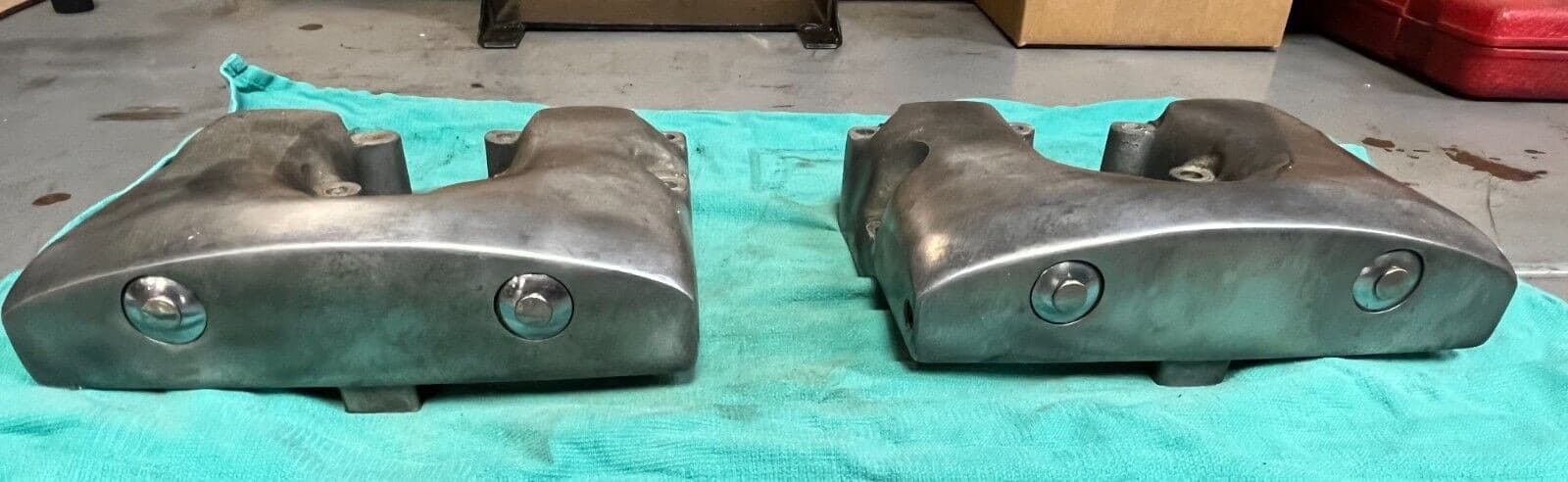 青緑の布の上に置いた、めっきの丸みのあるロッカーカバー2つ