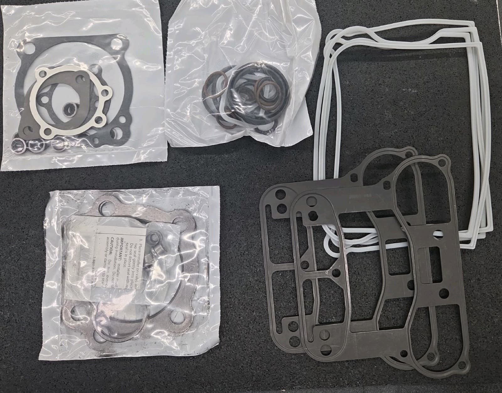 黒いマットの上に並べた、袋入りのガスケットの束。丸い穴の板や四角い枠の形の物がある