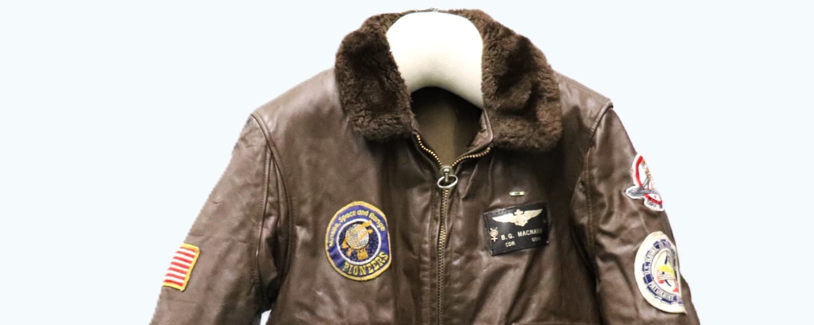 茶色の革のG-1の胸から上。こげ茶の毛皮の襟の下に、翼の徽章と「B.G. MACNABB」の文字の黒い名札、反対の胸に「PIONEERS」と書かれた丸いパッチがある