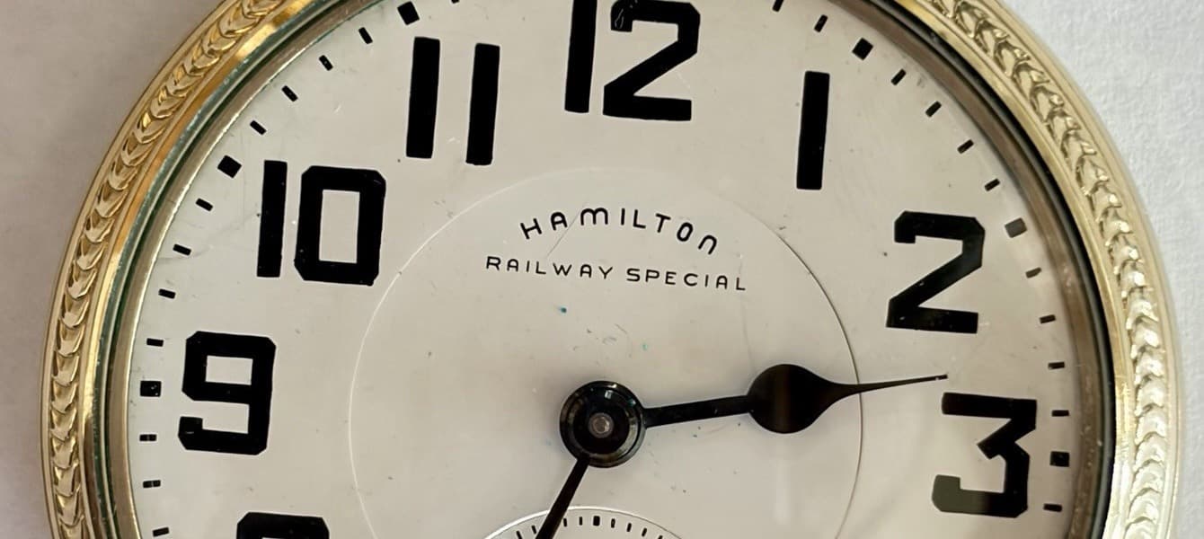 金色の懐中時計の白い文字盤の上半分。黒い太い数字の間に「HAMILTON」「RAILWAY SPECIAL」の文字がある