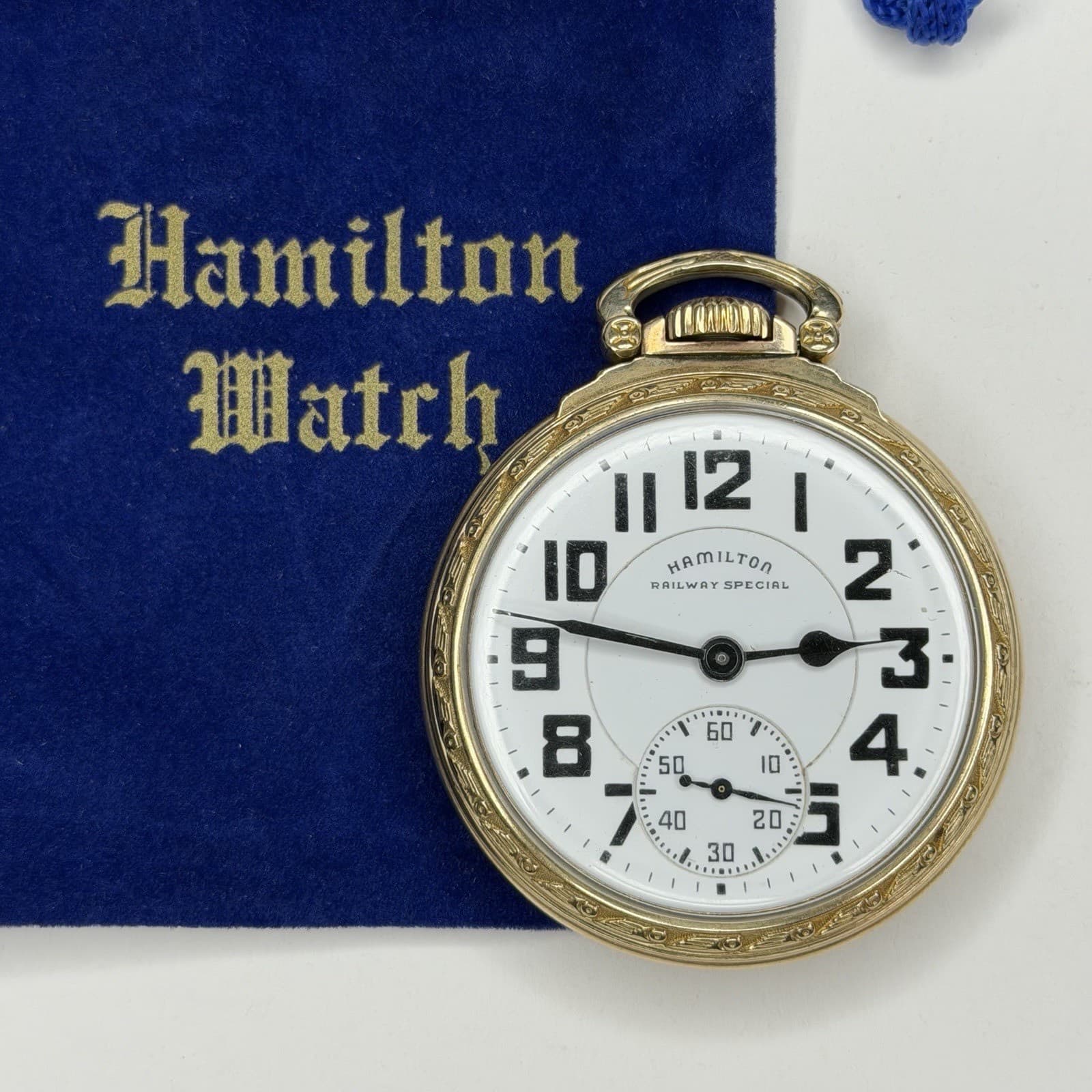 青い袋の上に置いた金色の懐中時計。白い文字盤に黒い太い数字と「HAMILTON RAILWAY SPECIAL」の文字がある