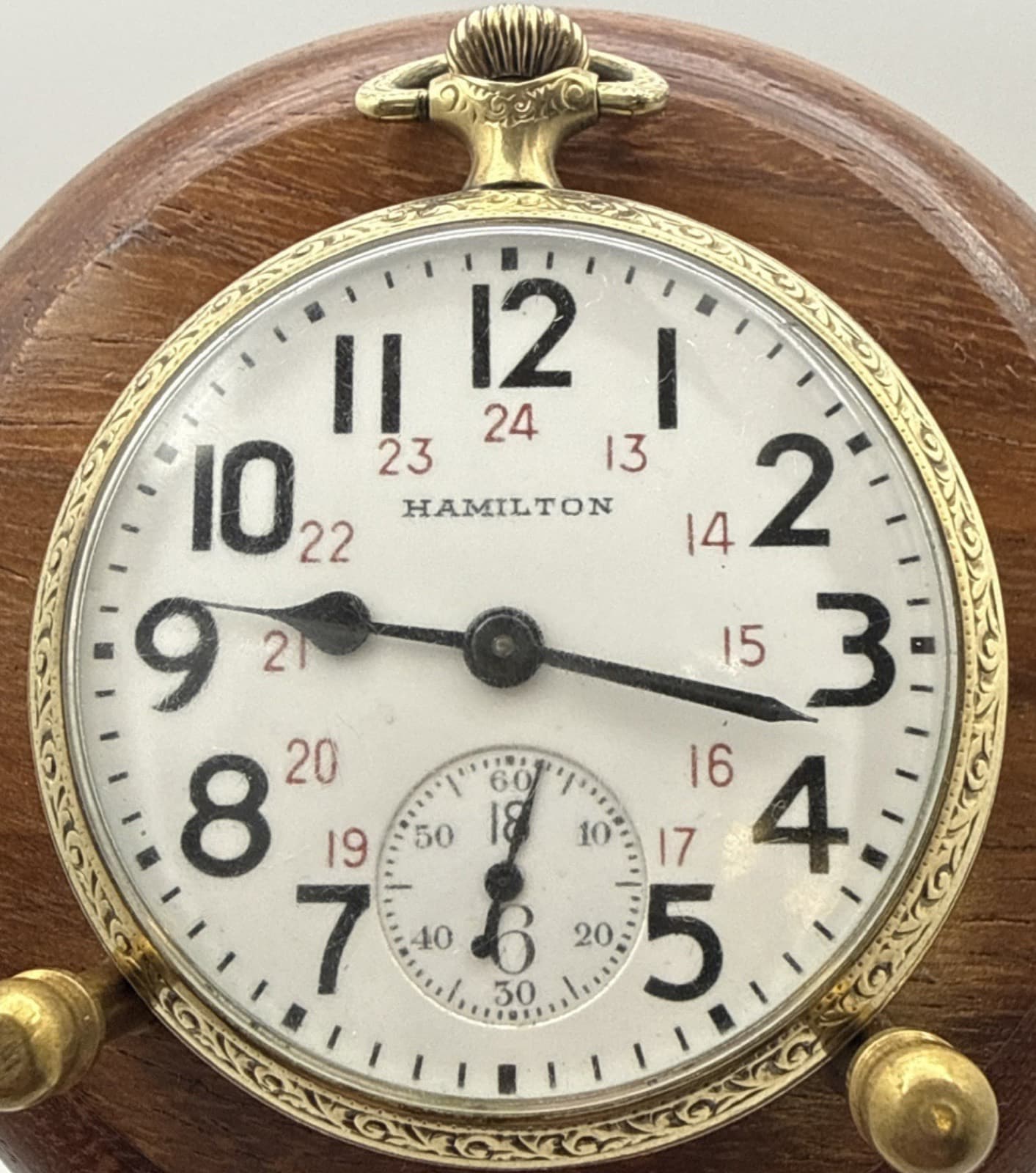 木の台に立てた金色の懐中時計。白い文字盤の黒い1〜12の内側に、赤い13〜24の数字が並ぶ