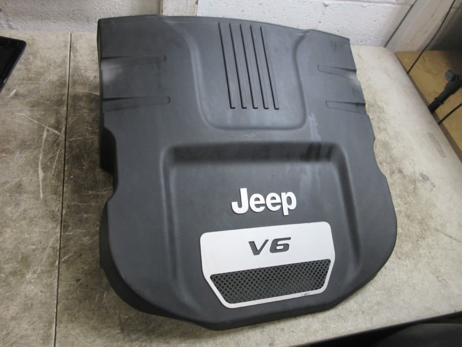 作業台に置いた黒い樹脂のエンジンカバー。Jeep の文字と、銀色の板に V6 の文字がある