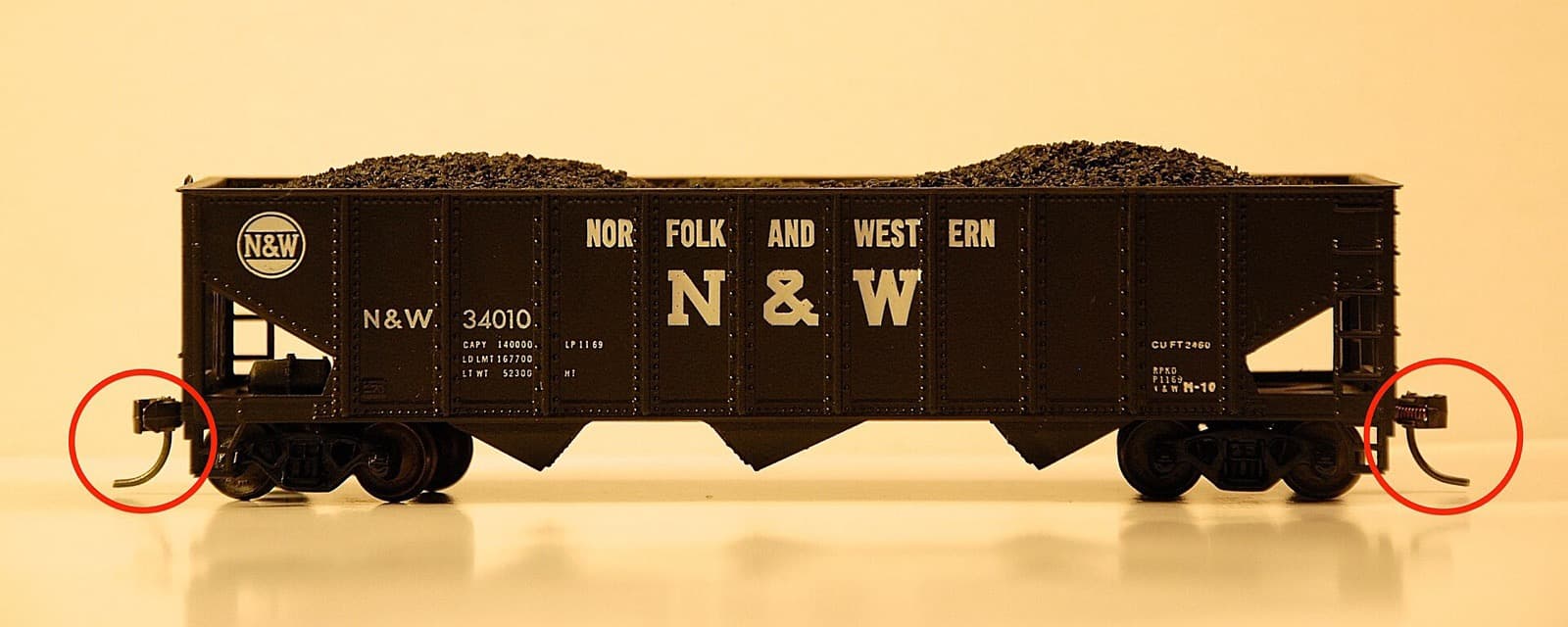 石炭を積んだ黒いホッパー貨車(N&W)の模型を真横から。両端の連結器と、そこから下に垂れた針金が赤い丸で囲まれている