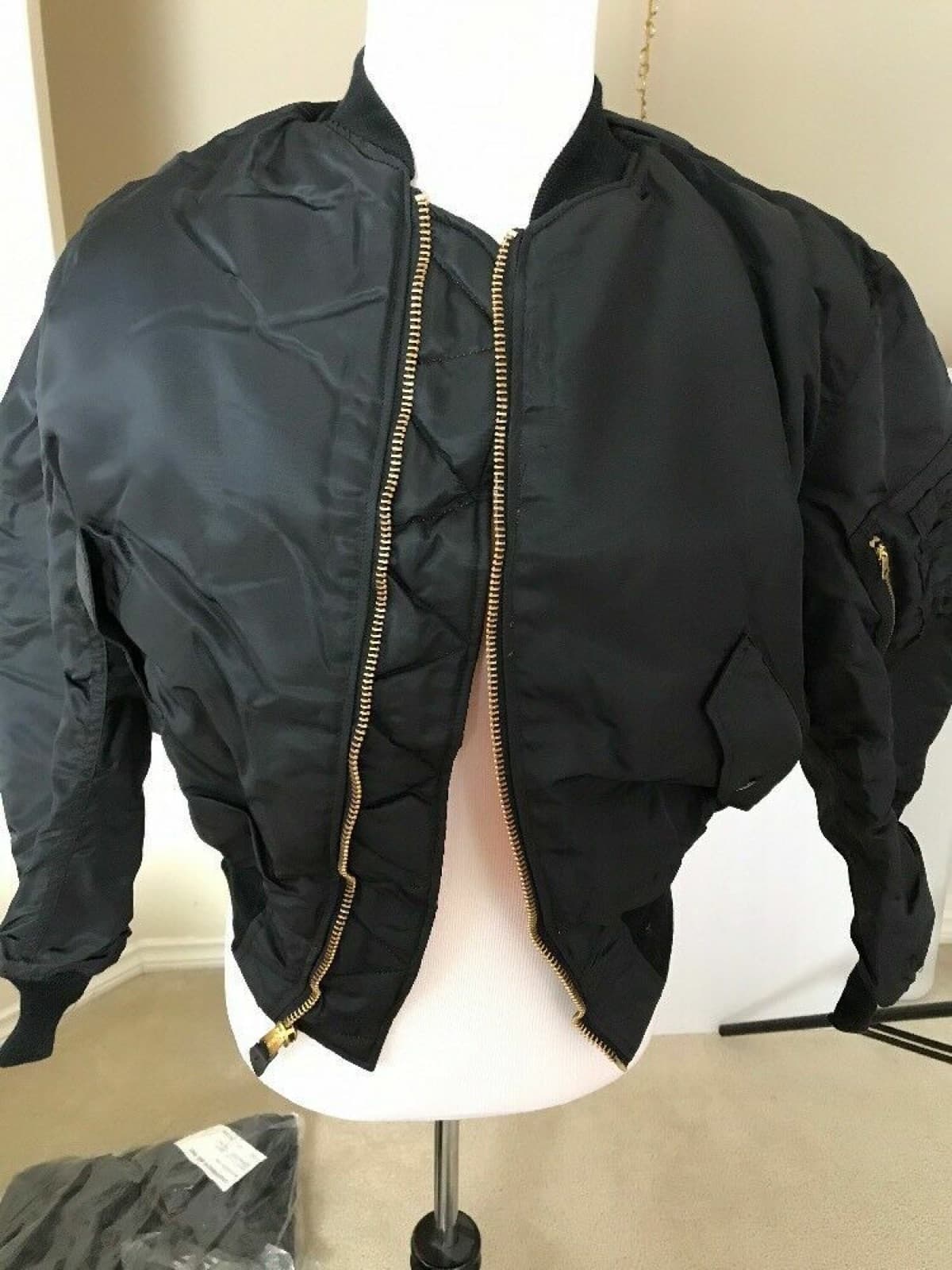 白いトルソーに着せた黒に近い色のナイロンの上着。前を開けて、金色のファスナーと左袖のポケットが見える
