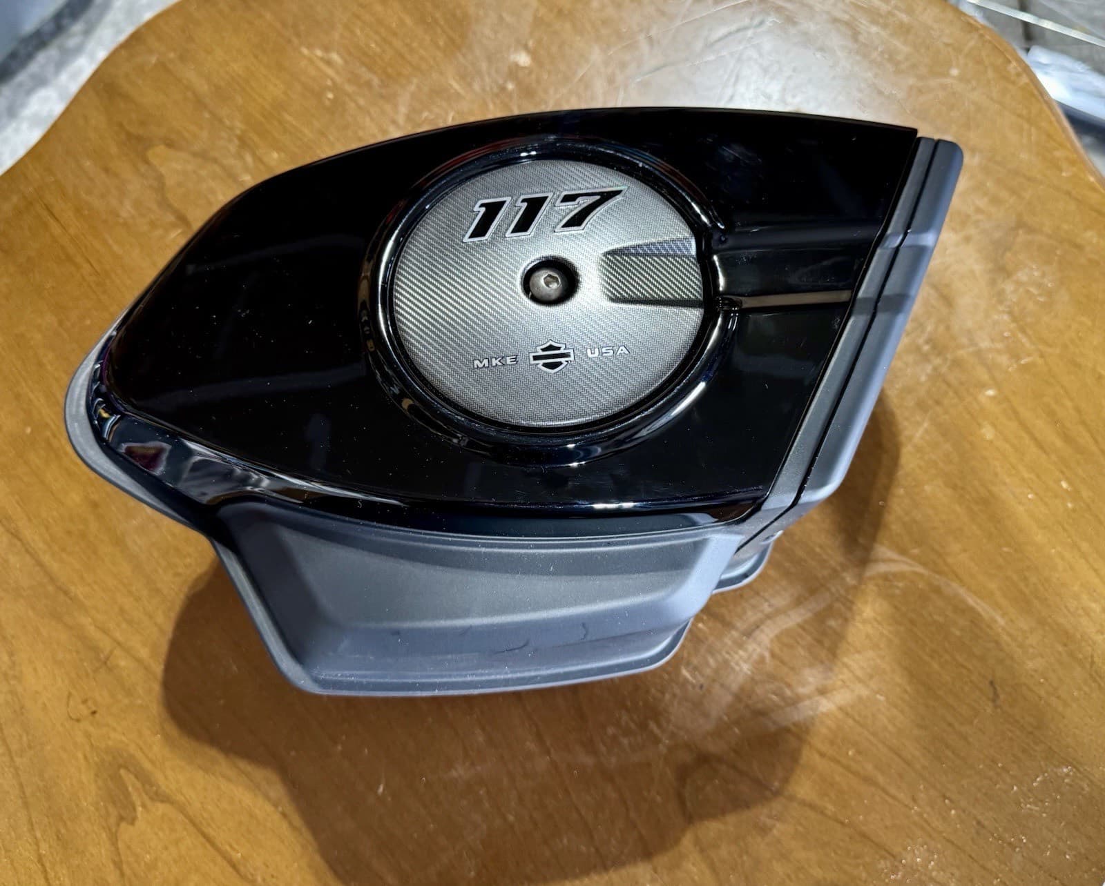 木の台に置いた、黒い光沢のエアクリーナーのカバー。丸い銀色の面に「117」の文字