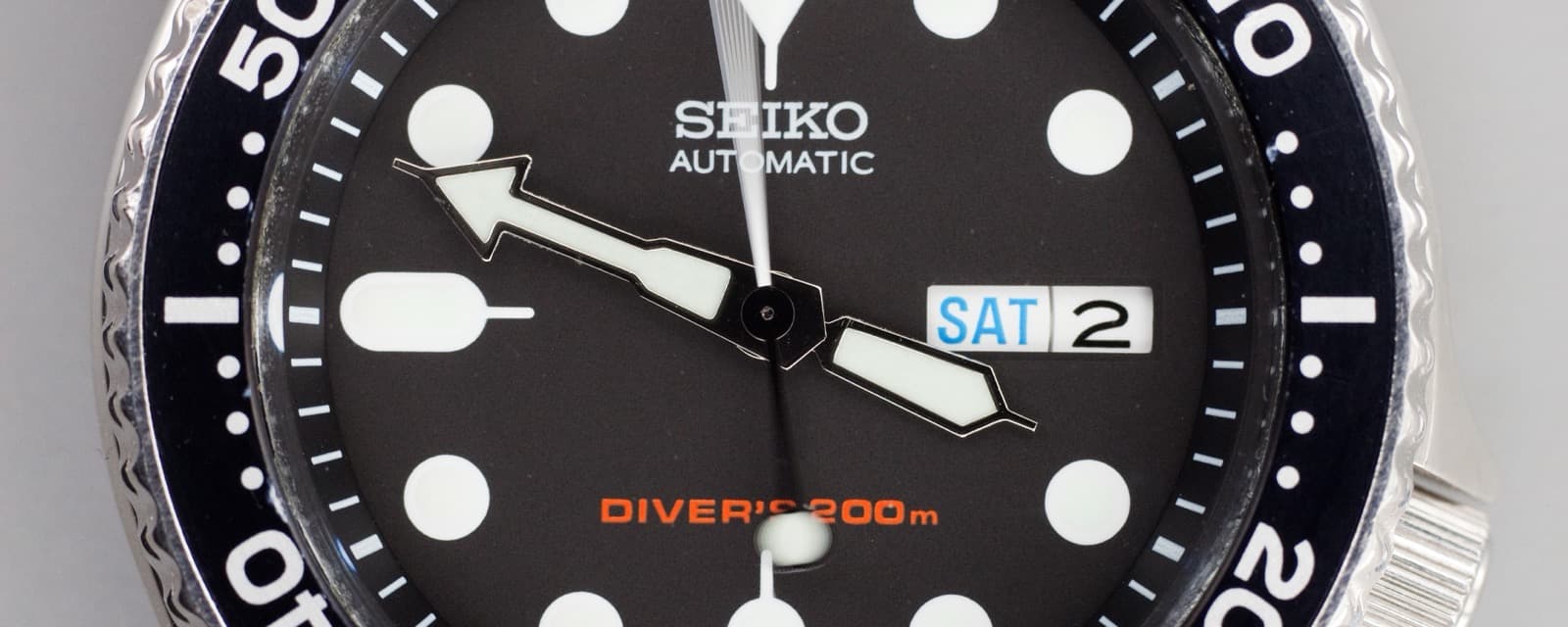 黒い文字盤のダイバーズを横長に切り出した写真。中央に「SEIKO」「AUTOMATIC」、右に曜日と日付の窓、下にオレンジの「DIVER'S 200m」、左右に黒い回転ベゼルの数字