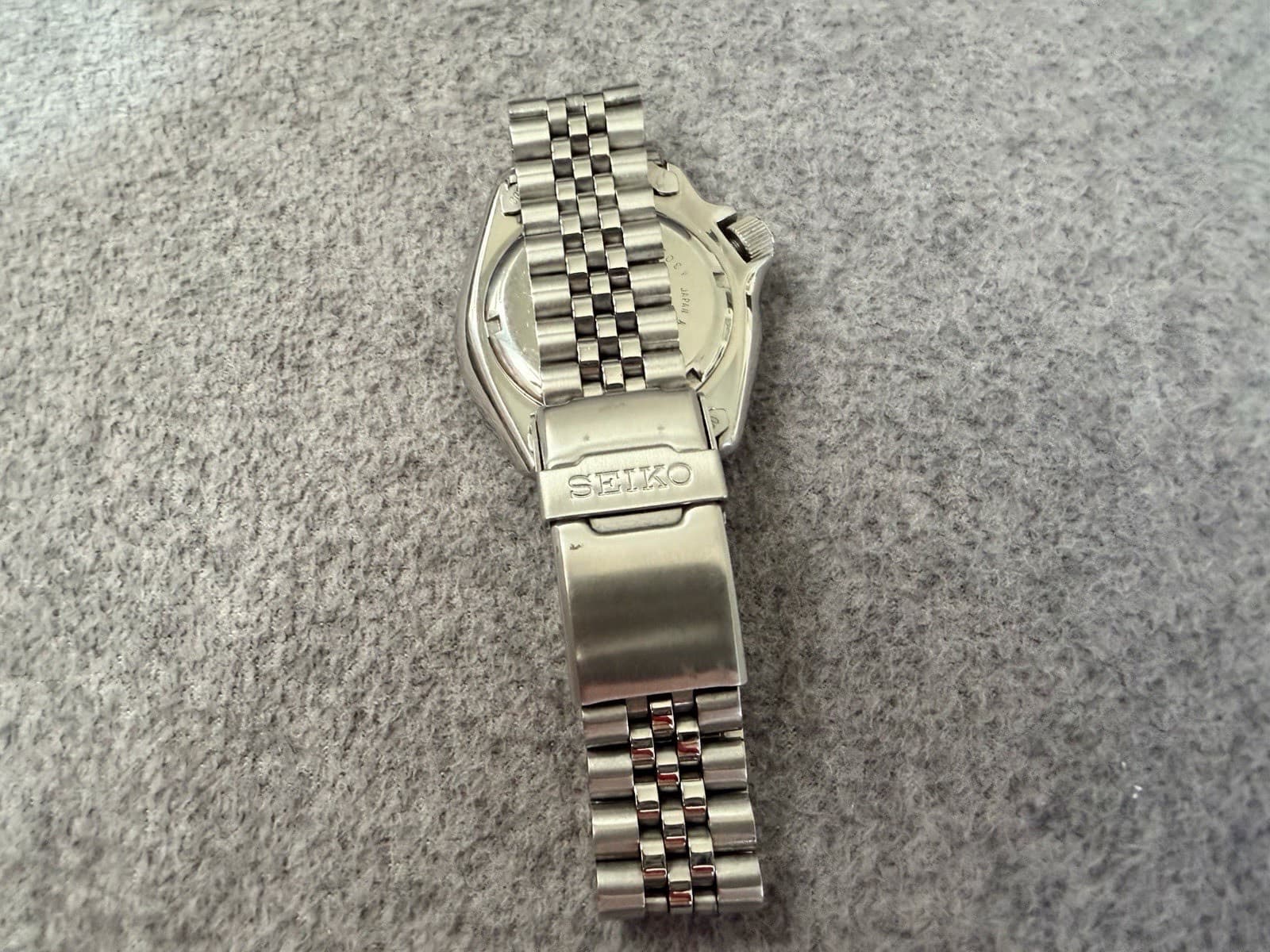 金属のブレスレットの付いた時計の裏ぶたの接写。中央に波の模様、周りに「SEIKO」「7S26-0020」「SCUBA DIVER'S」「430900」「JAPAN A」「STAINLESS STEEL」の刻印