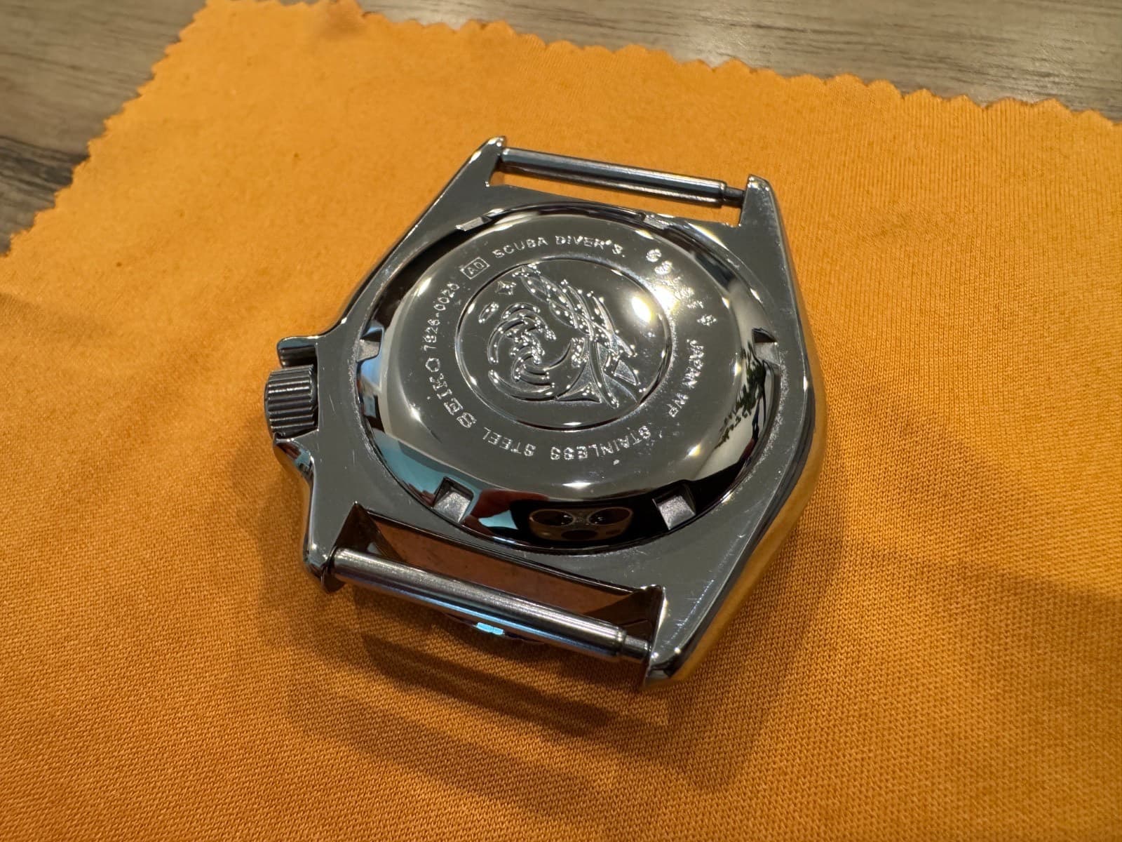オレンジの布の上に置いた時計の裏ぶたの接写。中央に波の模様、周りに「SCUBA DIVER'S」「646169」「JAPAN WR」「STAINLESS」の刻印