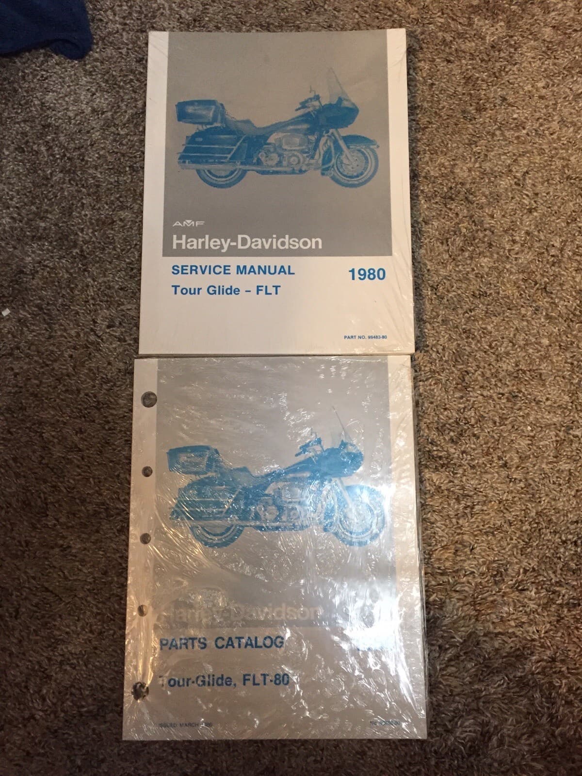 敷物の上に重ねた2冊の冊子。表紙に大きなカウルのバイクの絵と、1980 と Tour Glide の文字がある