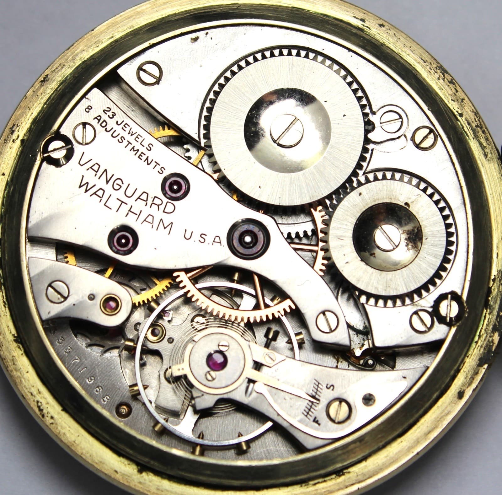 裏ぶたを開けた中のムーブメント。飾りの少ない銀色の受け板に「VANGUARD」「WALTHAM U.S.A.」「23 JEWELS」「8 ADJUSTMENTS」の刻印がある