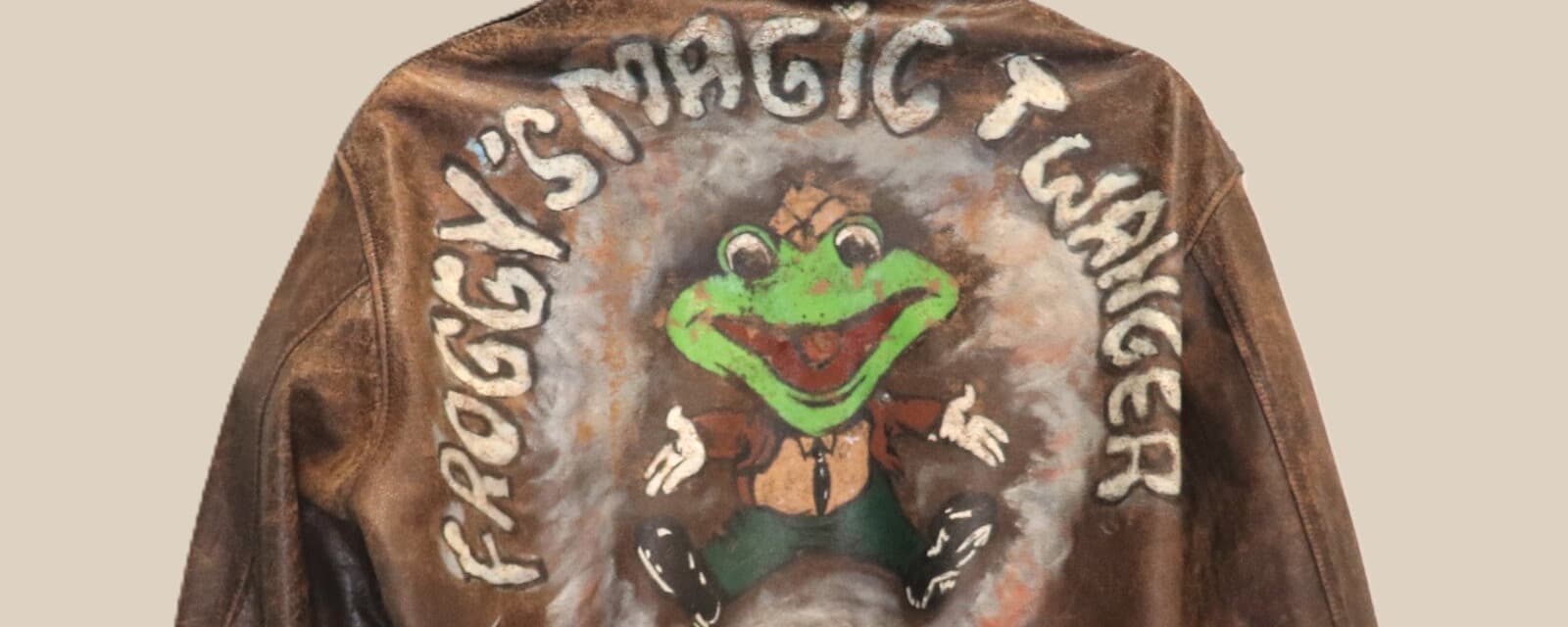 茶色の革のジャケットの背中。弧を描く「FROGGY'S MAGIC TWANGER」の白い文字の内側に、両手を広げた緑のカエルが手描きされている