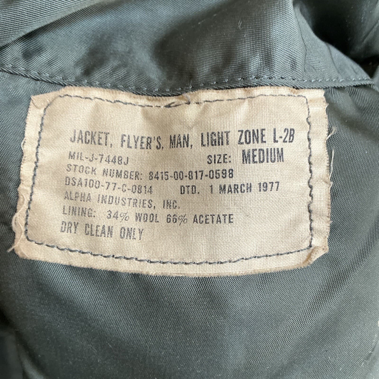 布のタグ。「JACKET, FLYER'S, MAN, LIGHT ZONE L-2B」「MIL-J-7448J」「STOCK NUMBER: 8415-00-817-0598」「DSA100-77-C-0814 DTD. 1 MARCH 1977」「ALPHA INDUSTRIES, INC.」と印刷されている
